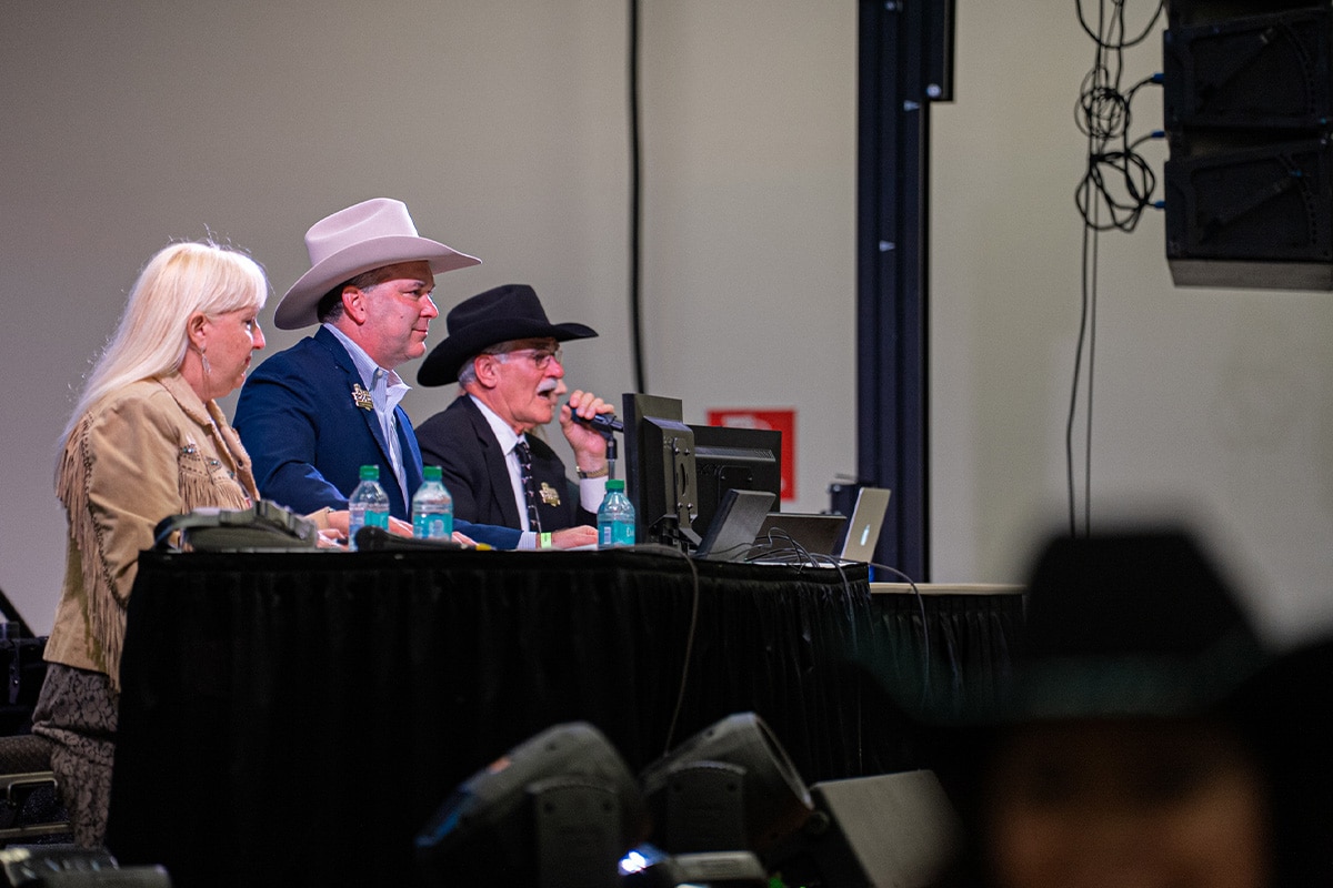 Three individuals in cowboy hats are seated at a table with microphones and laptops, engaged in a discussion or presentation.