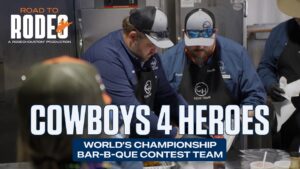 Cooks in blue shirts and aprons work at a barbecue station with a bold 'COWBOYS 4 HEROES' overlay filling the scene.